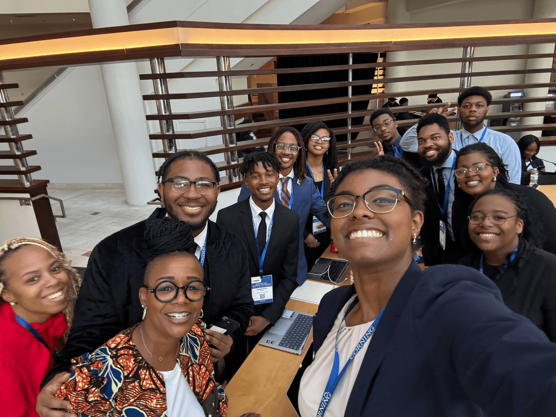 Group of smiling people taking a selfie in a modern indoor setting with conference badges visible.