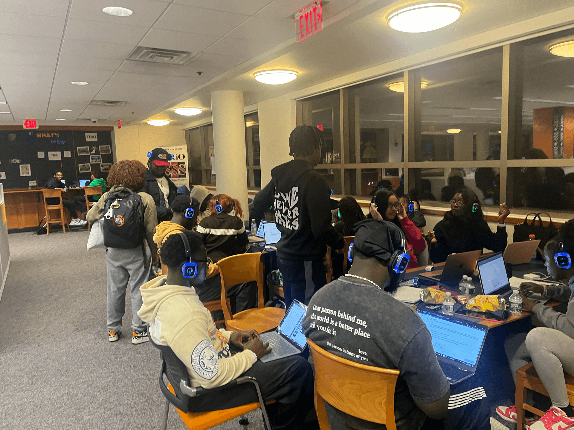 Students wearing headphones study together in a university lounge area with laptops and snacks.