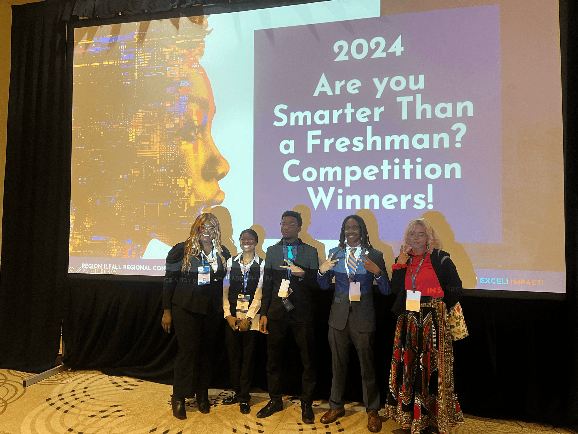 Group of five people standing in front of a screen showing 2024 competition winners announcement.